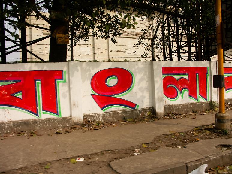 Bangla written out on a wall in Kolkata The letters for bangla or Bengali are written in red on a wall with barbed wire above along a sidewalk and a street in calcutta india
