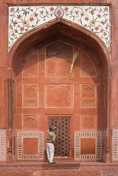 Sweeping the underside of the Arch A man with a very long broom sweeps in the underside of a red sandstone arch inlaid with marble and precious stone Mughal arch on the ground of the Taj Mahal in...