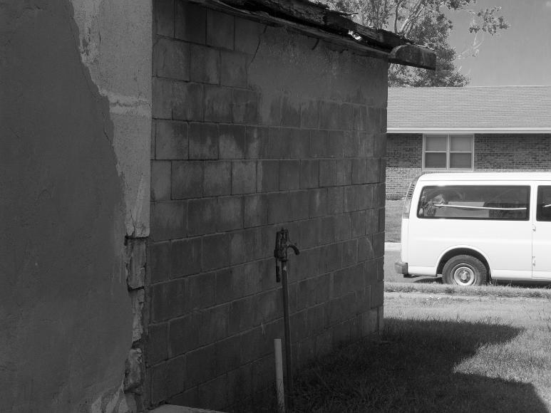 Spigot against a concrete shack Nicodemus Kansas Black and white photograph of a spigot in front of a cocrete block house that is partly spackled and a large passenger van parked out front, Nicodemus, Kansas