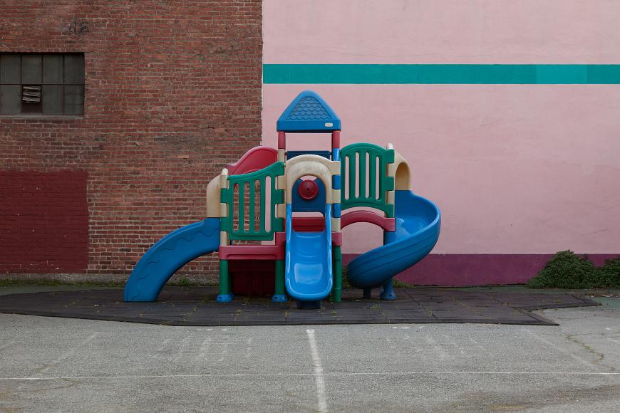 Scary Empty Playground empty plastic multicolored playground on black rubber mats against a brick wall and a pink and purple and turquoise painted wall
