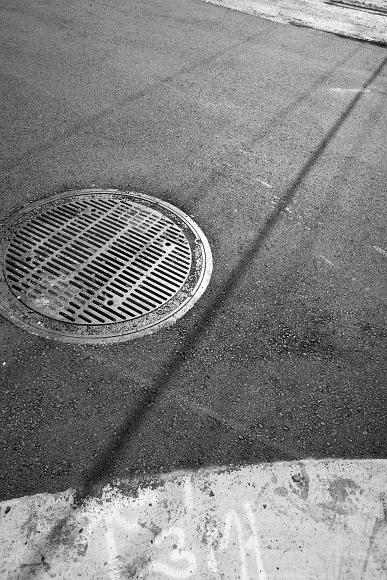 Street Patterns in the afternoon Power line shadows across very fresh asphalt and sewer manholes