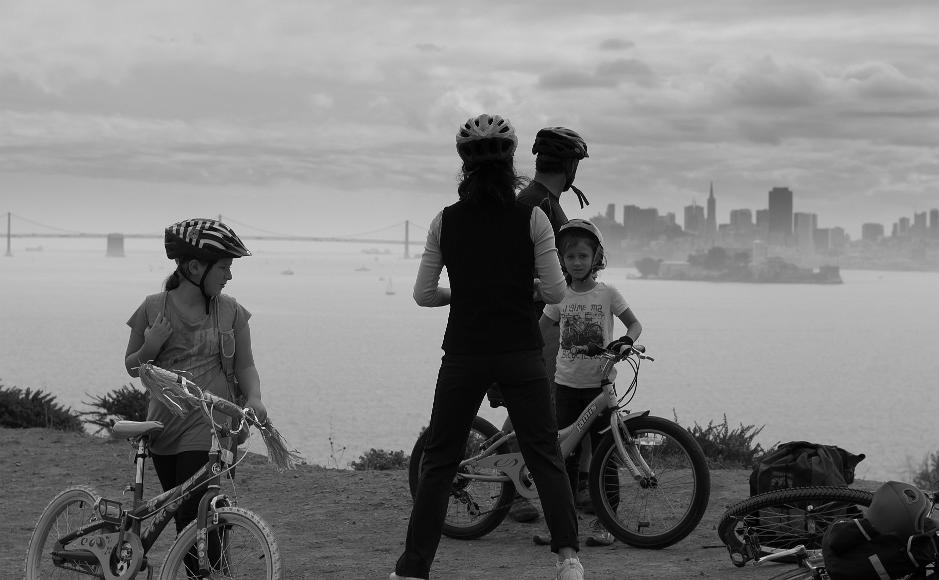 Family on bikes looks out Black and White of family on bikes with helmets on looking towards San Francisco the bay bridge and Alcatraz Island from Angel Island