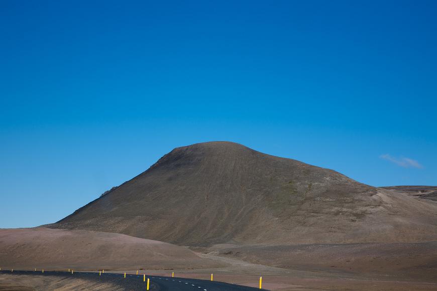 Bare dark colored hills with freshly asphaulted road with yellow markers in northern Iceland