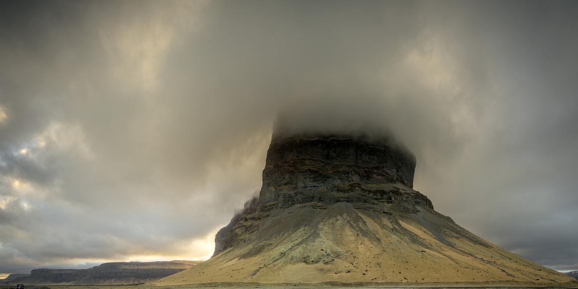 Clouds dance around trhe monolith Clouds dance around a volcanic seeming monotlith with other volcanic cliffs nearby, all lit by dramatic clouds and occasional sun, with clouds wrappingt...