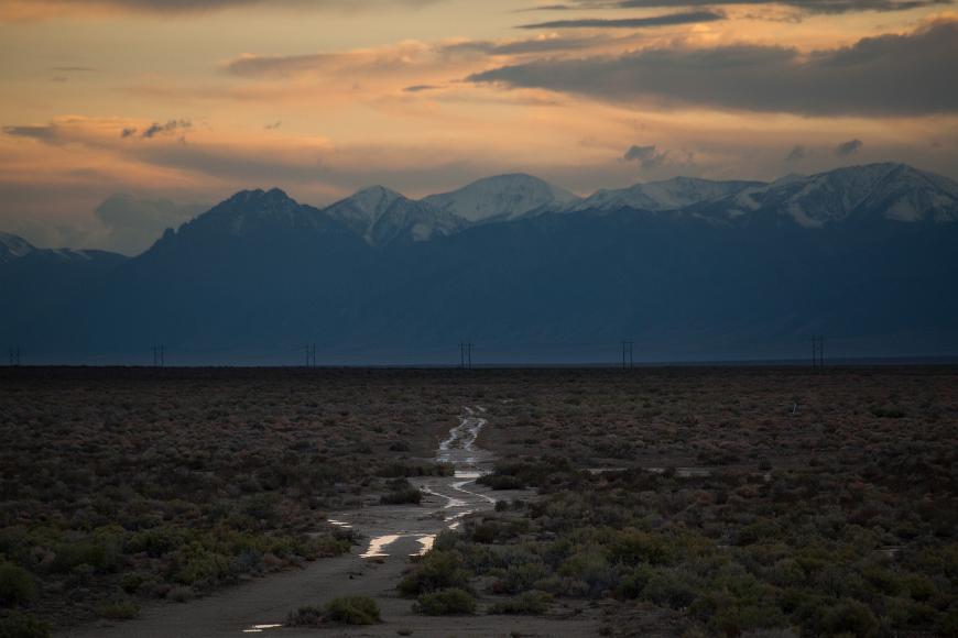 Water in road tracks against snow capped mountains at sunset After a rare rainfall in the desert, water lies in road tracks across the valley floor, with snowcapped mountains rising in the background, at dusk just after...