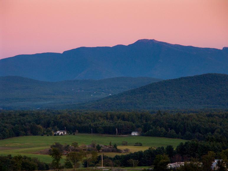 Sunset over Mt Mansfield from Fairfax VT a pink sky after sunset lies behind the blue-green ridge of mt mansfield, with smaller forested hills in the middle and rolling green farms and farmhouses in...